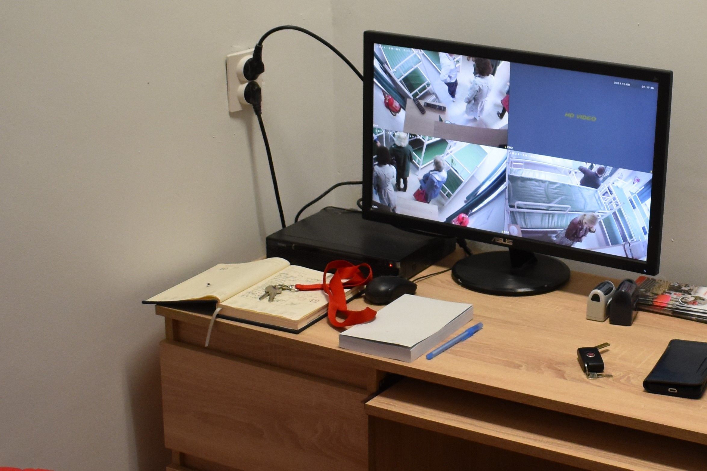Na biurku stoi włączony monitor komputera. Na ekranie widać widok pokazywany przez zainstalowane w pomieszczeniu kamery monitoringu.