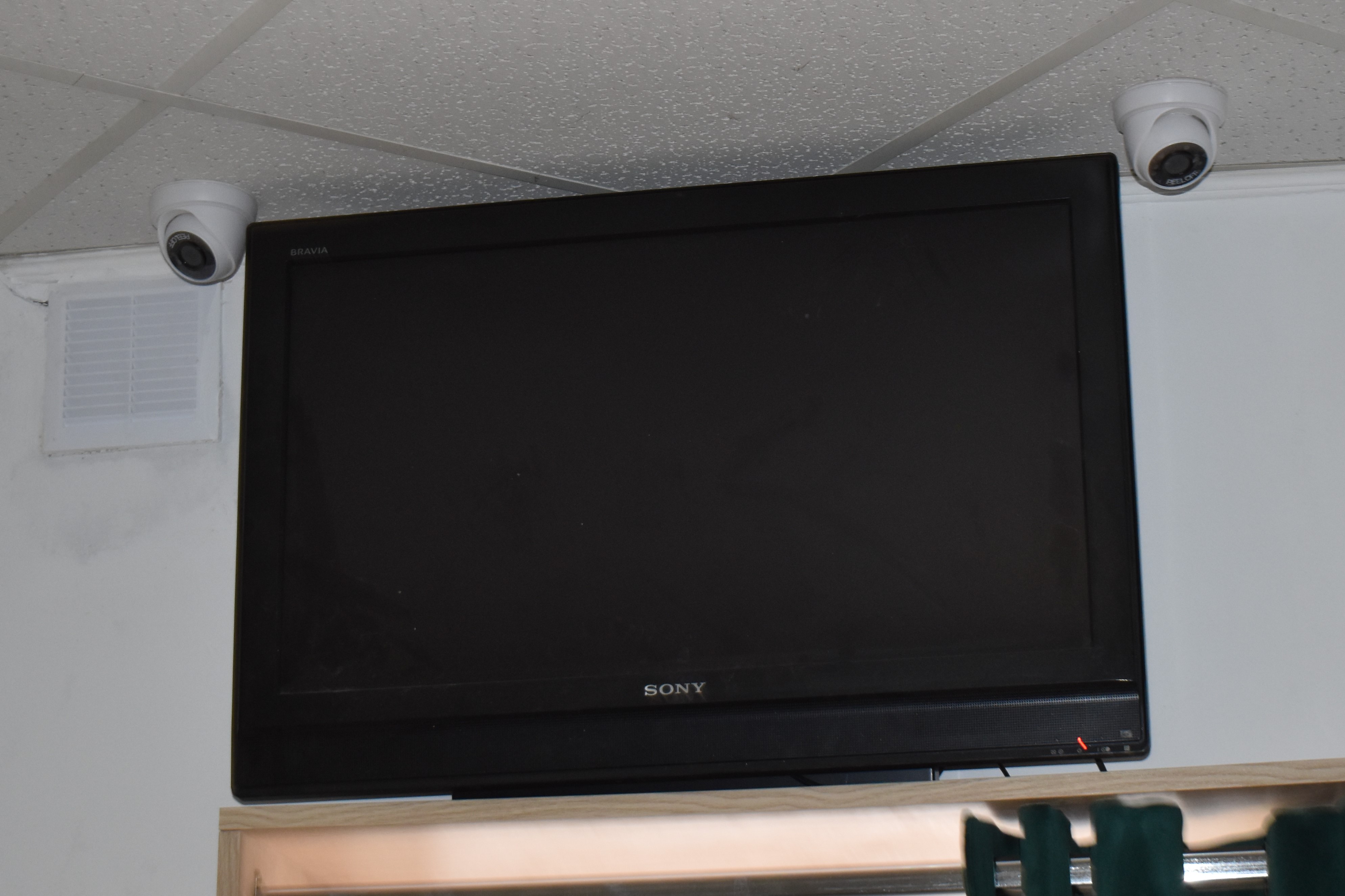 Telewizor zawieszony pod sufitem nad wejściem. Po obu stronach kamery monitoringu.