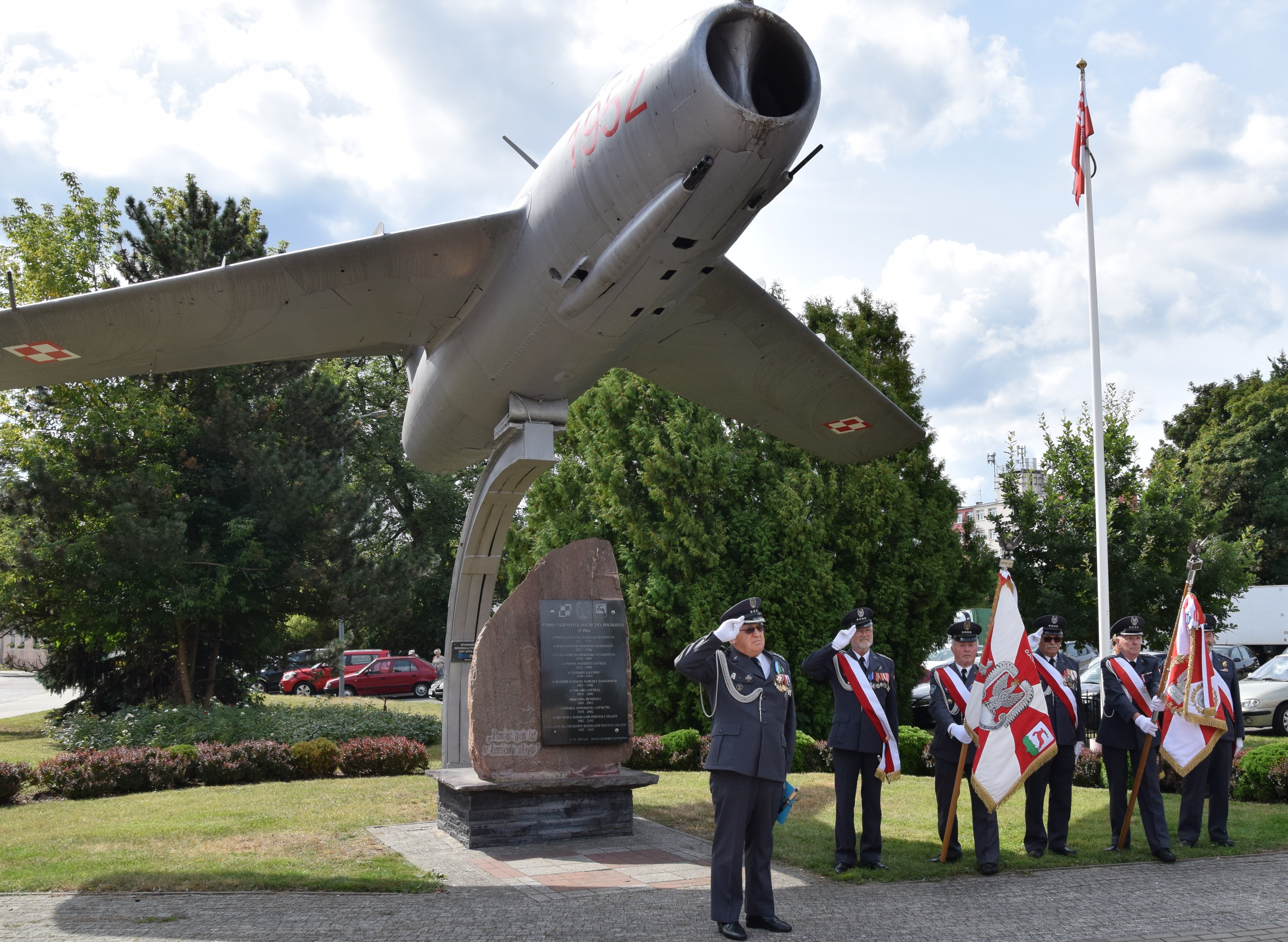 pod pomnikiem- samolotem - stoją lotnicy - prowadzący uroczystość pułkownik oraz poczet sztandarowy