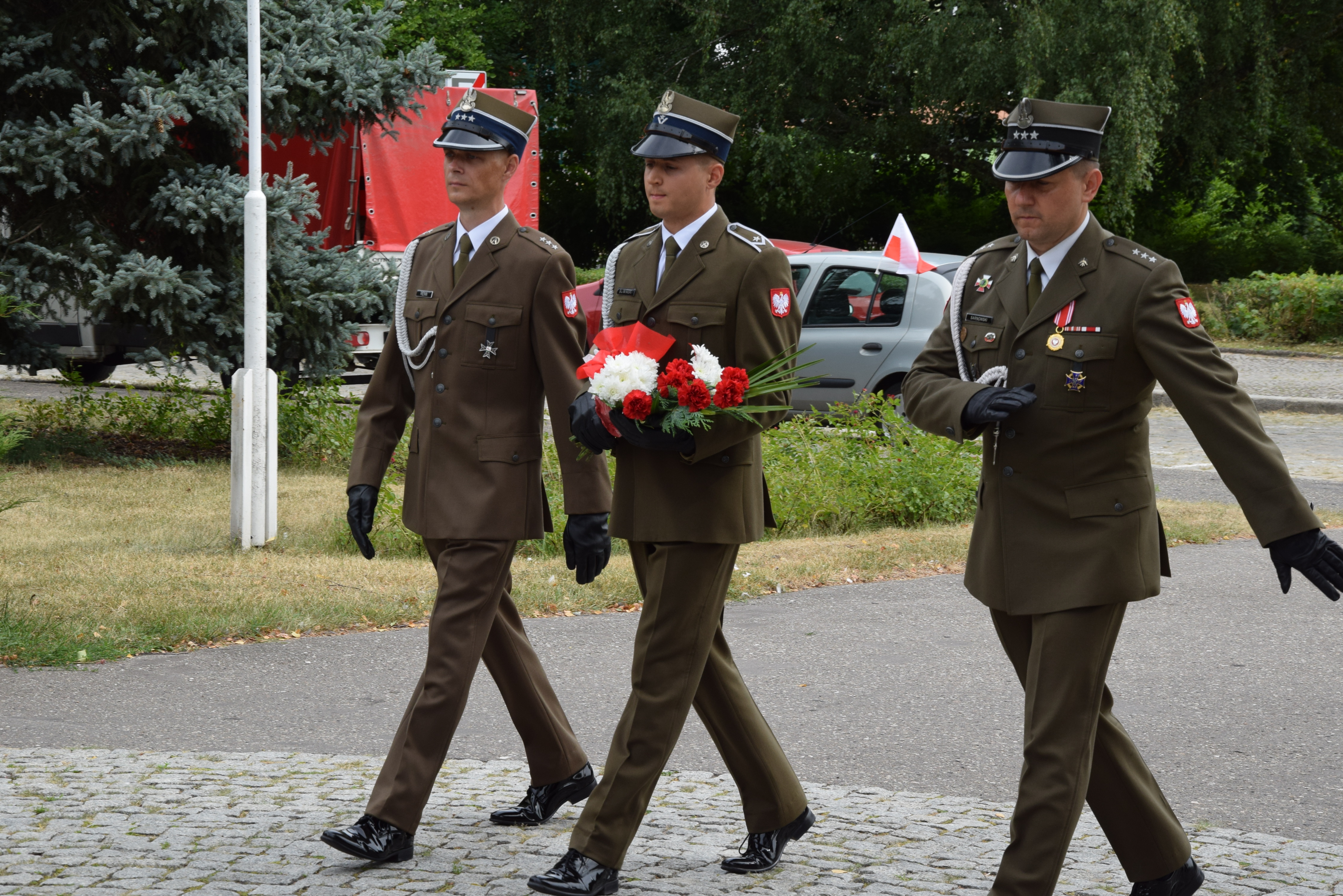delegacja skłądająca się z 3 żołnierzy maszeruje z kwiatami w stronę pomnika
