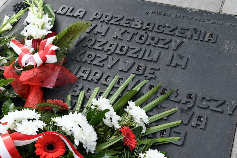 Tablica pomnika ofiar stalinizmu. Biało-czerwone kwiaty, wiązanki złożone pod pomnikiem.
