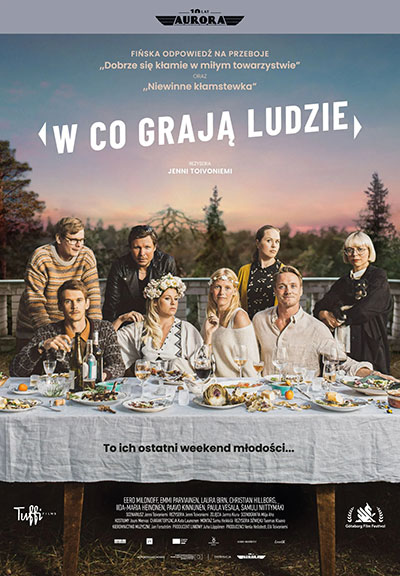 4 osoby siedzą za stołem, za nimi stoją 4 osoby, stół zastawiony jedzeniem